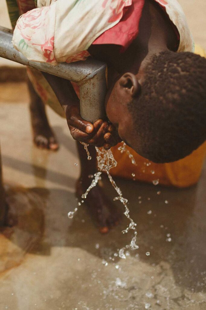 child drinking water from an outside tap